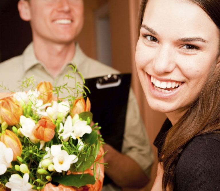 Smiling woman receiving a bouquet of flowers alongside delicious sweets from Transylvania Cakes, capturing a special moment of happiness and celebration.